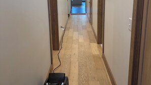 A hallway with wooden flooring, a charging station, and a view into a room with a sofa.