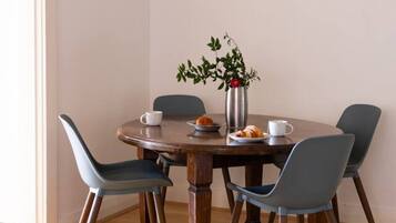 A dining area with a round wooden table, four chairs, a vase with a plant, and a framed picture on the wall.