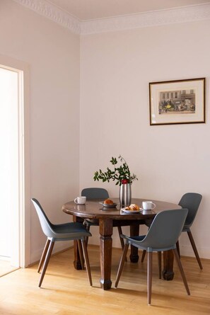 Un coin repas avec une table ronde en bois, quatre chaises, un vase avec une plante et un tableau encadré au mur.