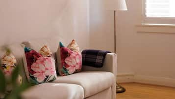 A living room with a sofa, two framed pictures, a lamp, and a window with blinds.