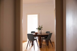 Un coin repas avec une table ronde, quatre chaises, un vase avec une plante et une porte donnant sur une autre pièce.