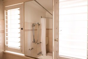 Une salle de bain avec une douche à parois de verre, des toilettes et une fenêtre avec des stores.