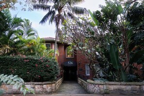 Un bâtiment en briques portant le numéro « 526 », entouré d’une végétation tropicale luxuriante.