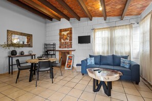A living room with a blue sofa, a round coffee table, a dining table with chairs, a fireplace, and a TV mounted on the wall. - Chic little house in San Miguel (San Miguel de Allende)