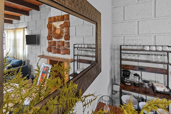 A modern interior with a brick wall, a wooden shelf with kitchenware, and a framed picture on a table.