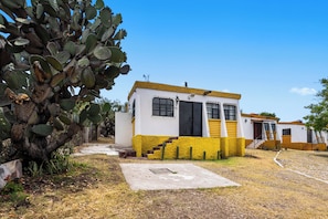 A small, single-story building with a yellow and white exterior, a visible door, and a staircase leading to the entrance.