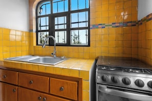 A kitchen with yellow tiles, a window, a sink, a stove, and wooden cabinets.