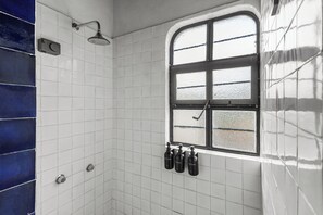 A bathroom with white tiled walls, a shower, a window, and four bottles of shampoo. - Chic little house in San Miguel (San Miguel de Allende)