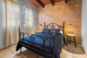 A bedroom with a bed, curtains, a window, a stone wall, and a tiled floor. - Chic little house in San Miguel (San Miguel de Allende)