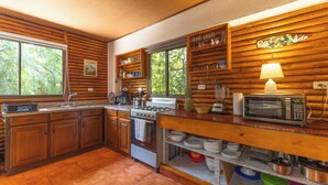 A kitchen with wooden paneling, a stove, microwave, and various kitchen utensils. - Casa Toucan,with a privat pool and a short walk from Bahia Ballena NP (Uvita)
