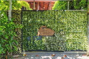 Un mur recouvert de feuilles vertes, une enseigne en bois avec du texte, et une clôture en métal.