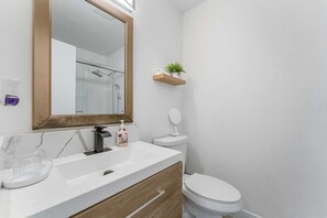 Ein Badezimmer mit weißem Waschbecken, einem Spiegel, einer Toilette und einem Regal mit einer Pflanze.