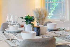 A dining table set with white plates, bowls, and glasses, accompanied by a potted plant and decorative items.