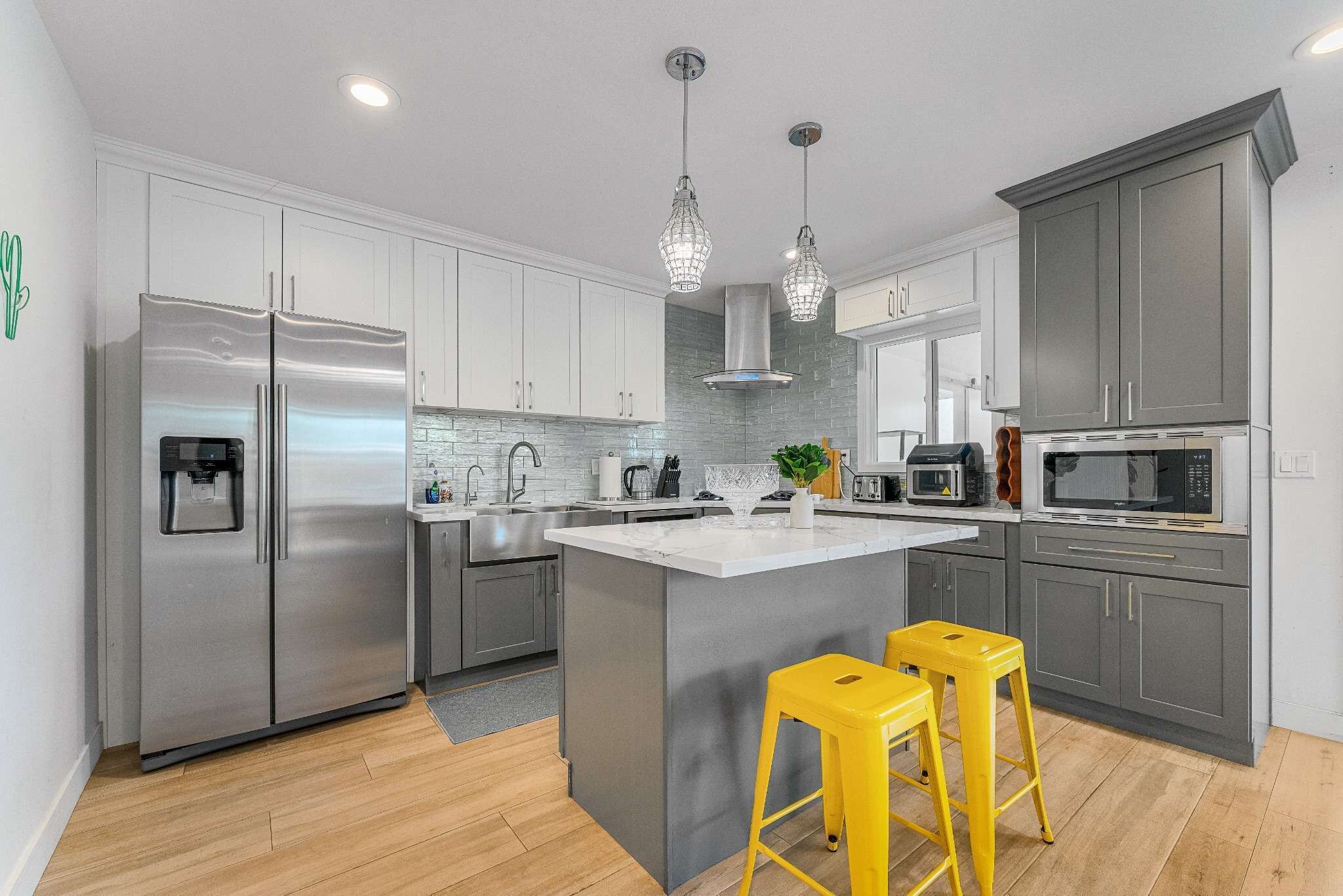 A modern kitchen with stainless steel appliances, grey cabinets, and a central island with yellow stools.