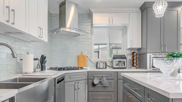 Una cocina moderna con gabinetes grises, electrodomésticos de acero inoxidable, una isla grande y una lámpara colgante.