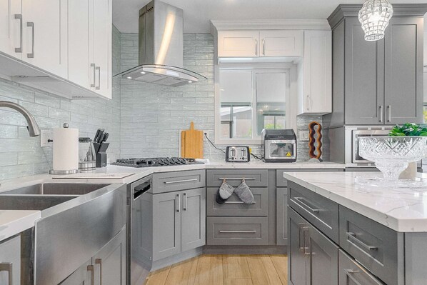 A modern kitchen with grey cabinets, stainless steel appliances, a large island, and a hanging light fixture.