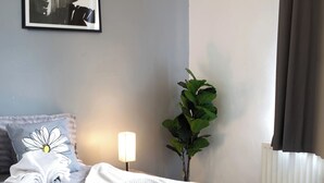 A neatly made bed with a plaid bed skirt, a bedside lamp, a potted plant, and a framed picture on the wall. - Room-double Room Perfect for Contractors (Wolverhampton)