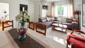 Ein Wohnzimmer mit einer Couch, einem Esstisch mit Stühlen, einer Vase mit Blumen und einem Bild an der Wand.
