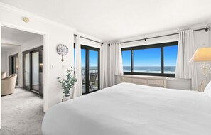 Ein Hotelzimmer mit einem großen Bett, Meerblick, einer Wanduhr und einer Pflanze.
