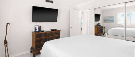A bedroom with a bed, a dresser, a television mounted on the wall, and a mirror.