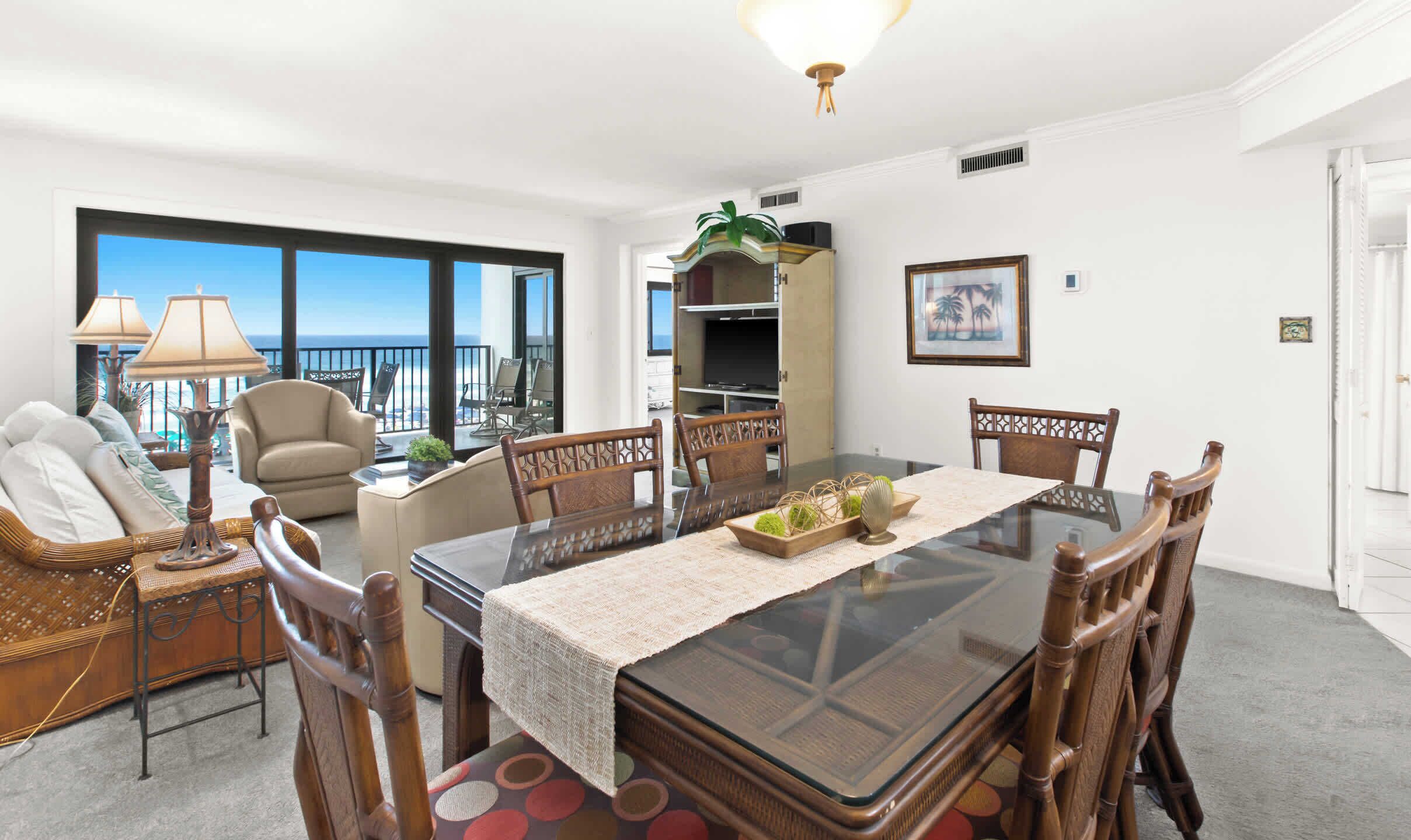 A dining area with a glass table, wicker chairs, a sofa, and a view of the ocean.