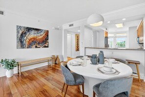 A modern dining area with a round table, grey upholstered chairs, and a large abstract painting on the wall.