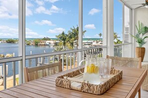 A wooden table with a woven tray, a pitcher of water, and glasses on a balcony overlooking a marina and ocean. - Isla Santorini | Islamorada Waterfront Condo, Ensuites, Pool, Hot Tub (Islamorada)