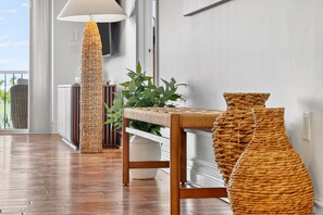 A wooden floor, a woven floor lamp, a woven bench, and a potted plant in a room with white walls.