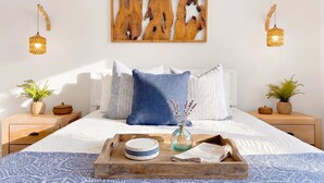 Een keurig opgemaakt slaapkamer met een bed, kussens, een dienblad met spullen, nachtkastjes met planten en wandlampen.