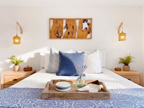 Um quarto bem organizado, com cama, almofadas, um tabuleiro com objetos, mesas de cabeceira com plantas e luminárias fixadas na parede.