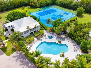 Um imóvel residencial com piscina, quadras de tênis e uma casa de dois andares com varanda.