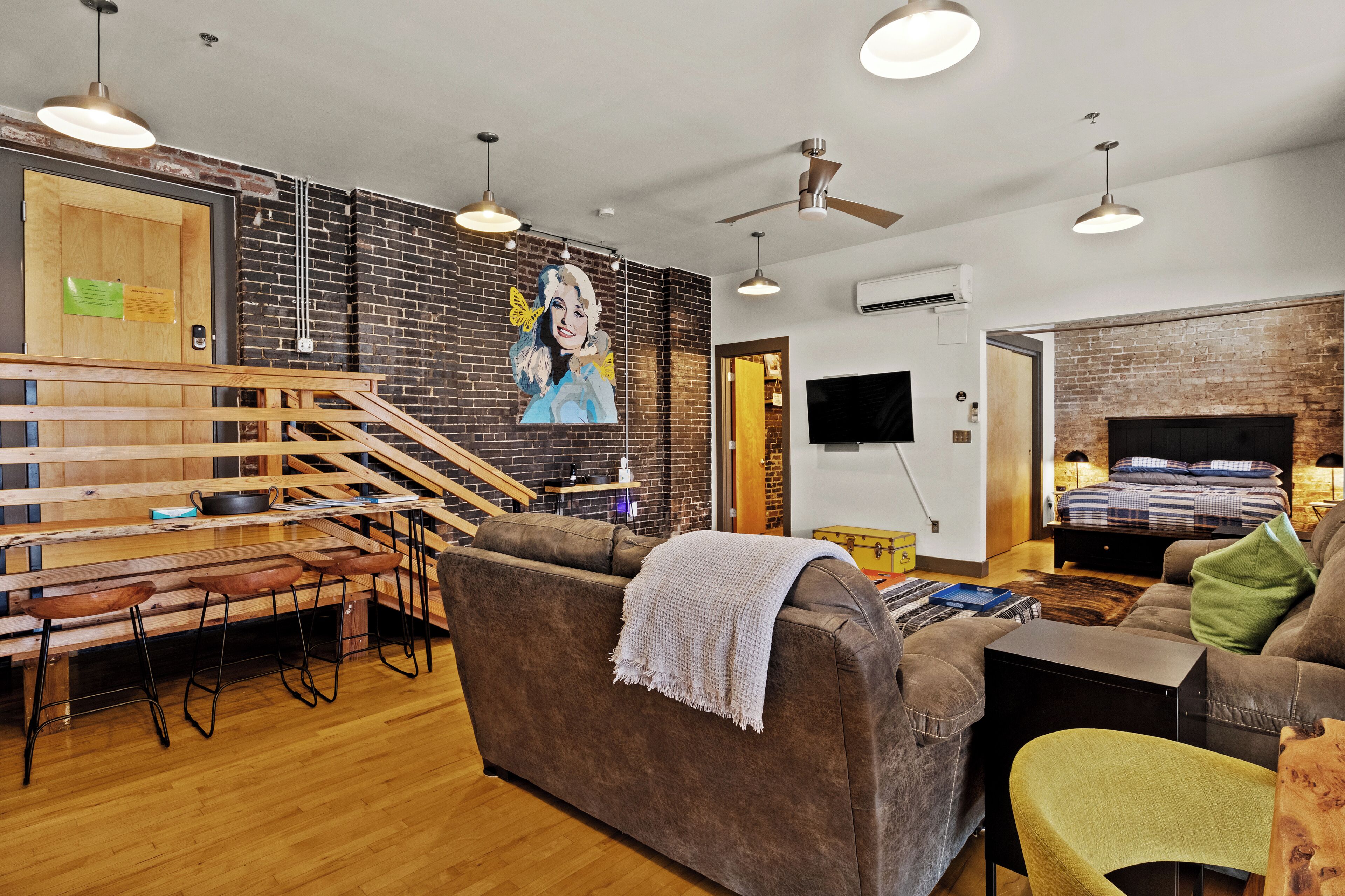 Un intérieur moderne avec un mur en briques, une fresque murale, un coin repas avec des meubles en bois, un canapé et un téléviseur.