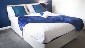 Ein ordentlich bezogenes Bett mit einem weißen Kopfteil, einer blauen Decke und zwei türkisfarbenen Kissen.