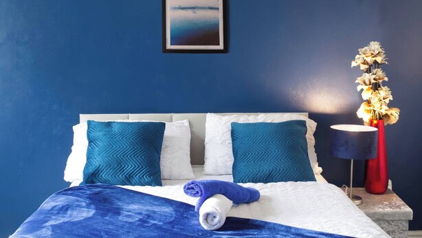 Ein Bett mit blauer Decke, weißen Kissen und einem zusammengerollten Handtuch.