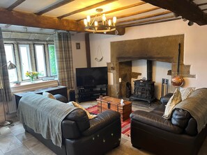 A living room with a fireplace, leather sofas, a TV, and a stone wall. - 17th Century Cottage, Log Burner & Hidden Garden (Laycock)