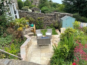 A stone wall, a small shed, and a patio with wicker furniture. - 17th Century Cottage, Log Burner & Hidden Garden (Laycock)
