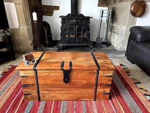 A wooden chest with metal clasps in a room with a stone wall, a fireplace, and a patterned rug. - 17th Century Cottage, Log Burner & Hidden Garden (Laycock)