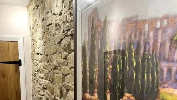 Un tableau encadré représentant une cour intérieure avec des colonnes et un bâtiment, accroché à un mur en pierre à la texture particulière.