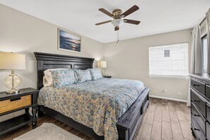 A bedroom with a bed, bedside tables, a ceiling fan, a window with blinds, and a dresser.