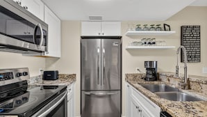 Una cocina moderna con electrodomésticos de acero inoxidable, encimeras de granito y armarios blancos.