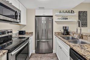A modern kitchen with stainless steel appliances, granite countertops, and white cabinetry. - 2 Bedroom Oceanfront Condo with Pool! (St. Simons Island)