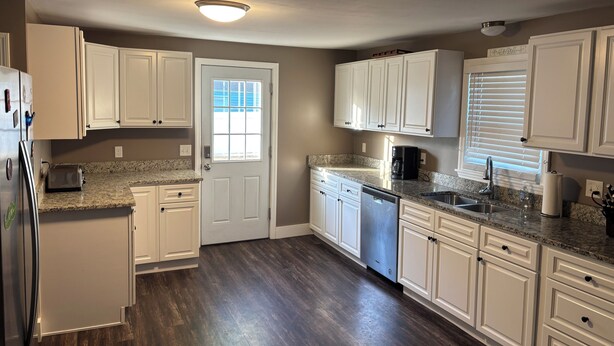 A kitchen with white cabinets, a granite countertop, a dishwasher, and a refrigerator.