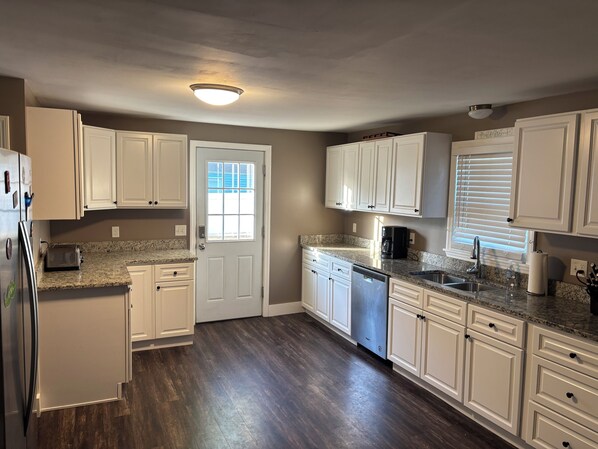 A kitchen with white cabinets, a granite countertop, a dishwasher, and a refrigerator.