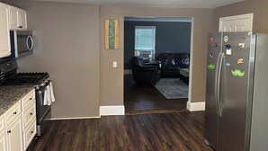 A kitchen with a stove, microwave, refrigerator, and a dining area with a dark wood floor.
