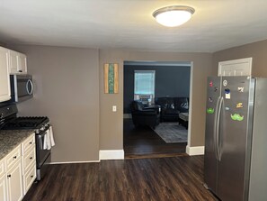 A kitchen with a stove, microwave, refrigerator, and a dining area with a dark wood floor.