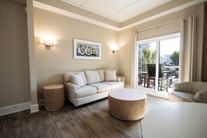 A living room with a sofa, two round ottomans, a painting, and a view of the outdoors through a sliding glass door.