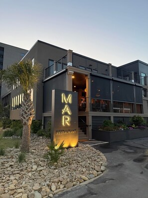 Een modern gebouw met een bord waarop 'MAR RESTAURANT' staat en een palmboom op de voorgrond.