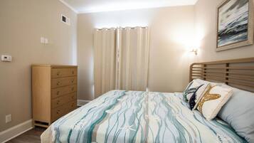 A bedroom with a bed, a dresser, a window with curtains, and a wall-mounted light fixture.