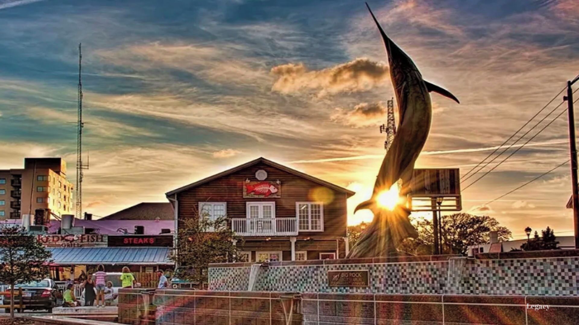 Ein Holzkonstrukt mit einem Schild für ein Steakhaus, einer hohen Skulptur und einem Sonnenuntergang im Hintergrund.