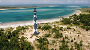 Um farol com um padrão de diamante distinto, rodeado por uma praia e vegetação rasteira.